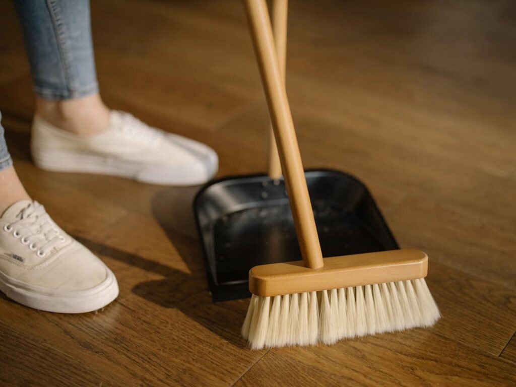pexels-photo-4108715 Close-up of cleaning process with broom and dustpan beside sneakers on a wooden indoor floor.
